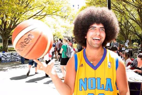 Student dressed in sports gear balancing a basketball on the tip of one finger