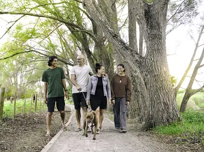 A whānau of 4 walking their dog down a nature path.