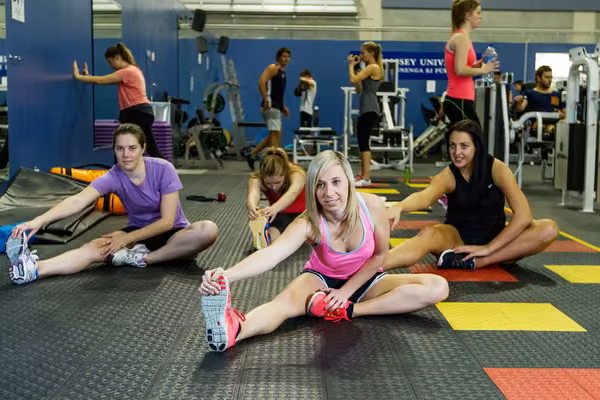 Students sitting on the gym floor doing leg stretches in the Auckland Recreation Centre