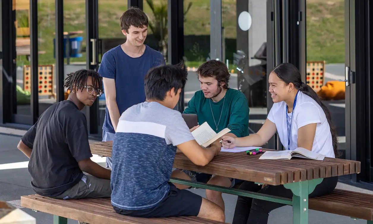 5 students sitting on a picnic table outside.