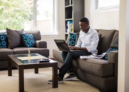 One person sitting on a couch typing on a laptop which is balanced on their knee