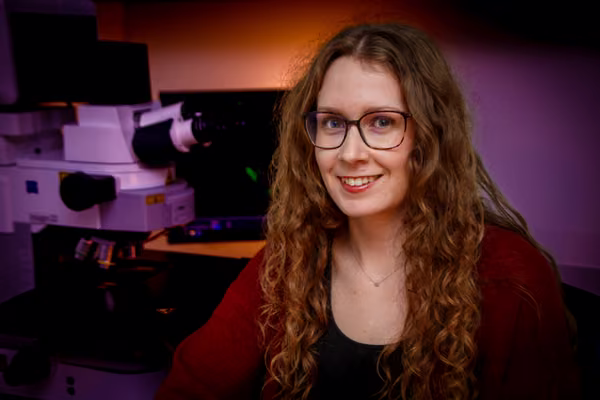 Dr Hannah Hawley sits in front of a microscope in a lab.