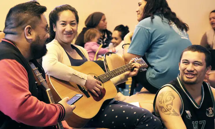 Person strumming a guitar with two other students smiling and talking