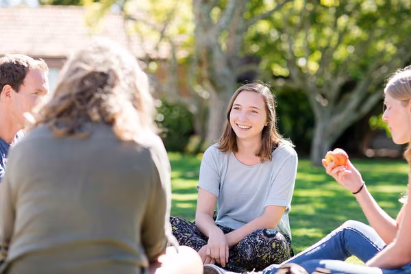 Four students sitting on the grass, smiling and talking