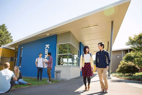 Small groups of students standing and sitting on the ground outside the Manawatū Halls