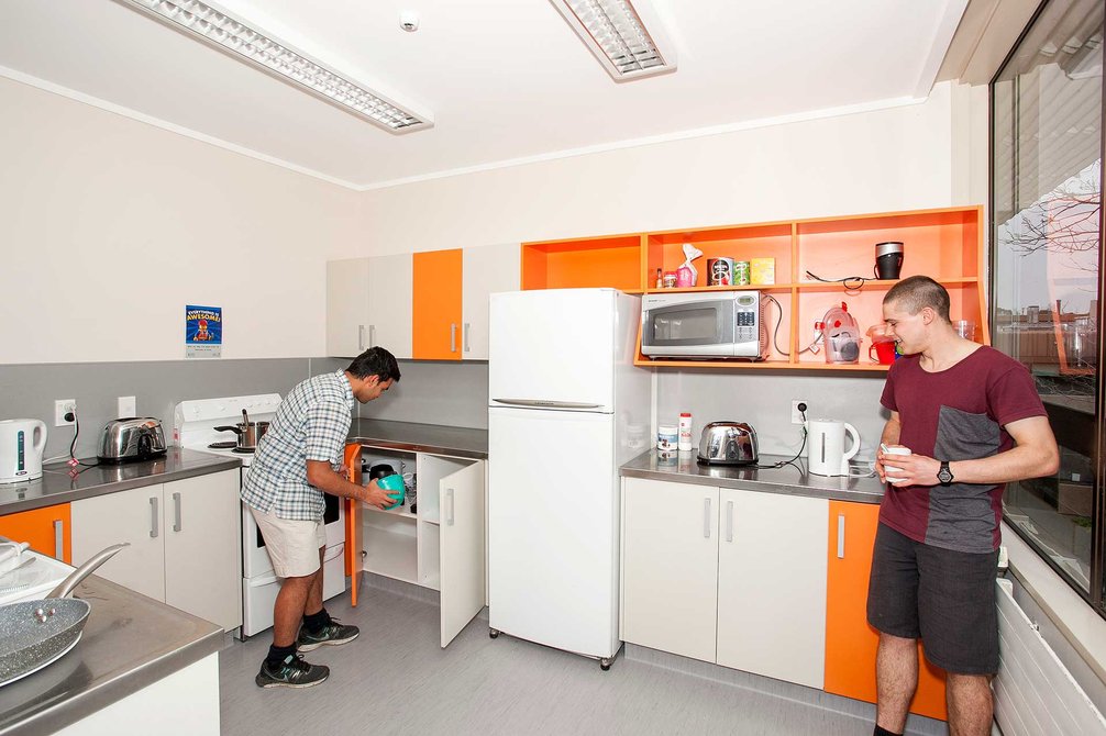 Colombo Hall's kitchen with cupboards, fridge and oven, and two students preparing a hot drink