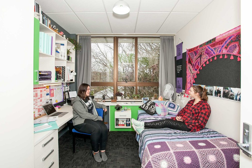 Two students sitting in a Colombo Hall single bedroom with a bed, desk and chair