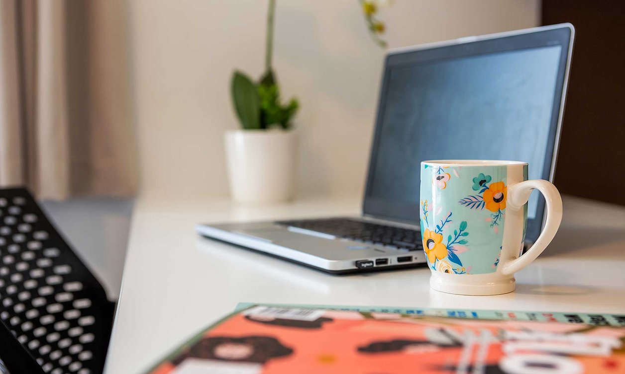 Close-up of laptop on a desk with a coffee mug and a plant