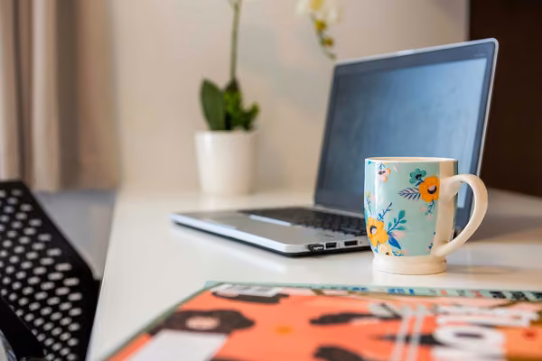 Close-up of laptop on a desk with a coffee mug and a plant