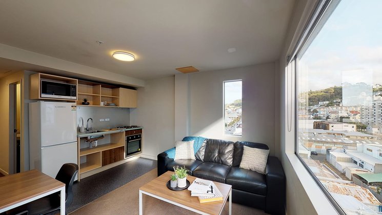 Lounge in The Cube apartment, with fridge, kitchenette, tables and couch and Wellington city views