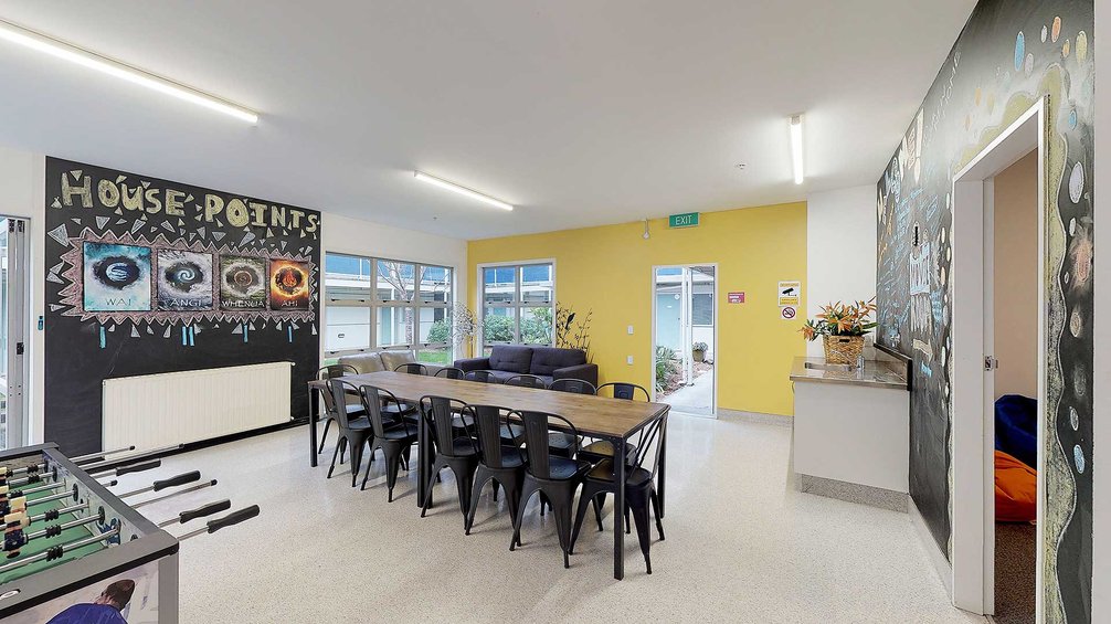 Interior of Kāinga Rua common room, with a large dining table and chairs
