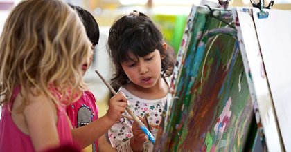 Three children holding paint brushes while painting at Massey University Childcare