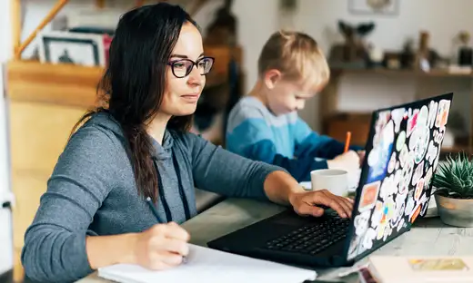 Woman studying at home next to child drawing.