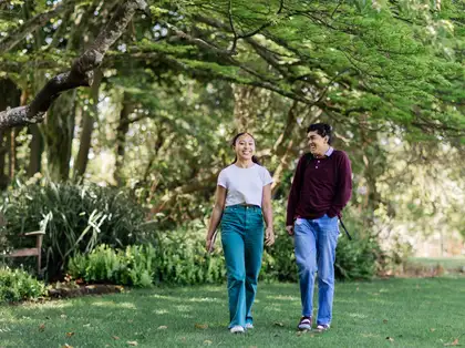 Two students walking on campus with surrounding green trees