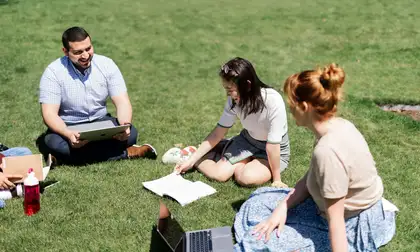 3 students sitting on grace studying on summer day.