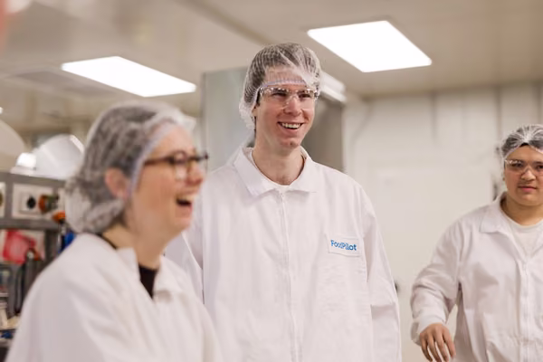 three students in white coats and hair nets smiling