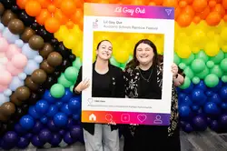 Photo booth at Lil Gay Out featuring two people infront of rainbow balloon display holding an Instagram type frame.