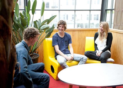 Three students inside, sitting around a table, laughing