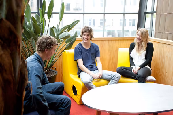 Three students inside, sitting around a table, laughing