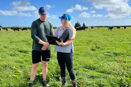 woman and man standing in field of cows looking at documents in a binder