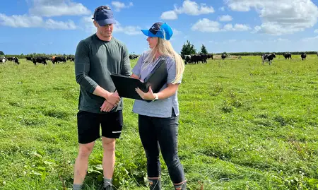 woman and man standing in field of cows looking at documents in a binder