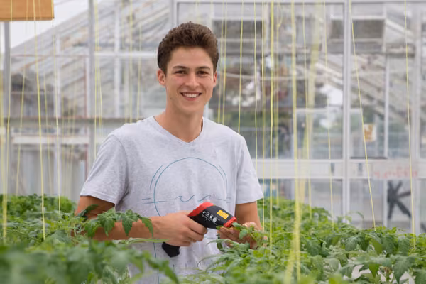 man smiling standing in greenhouse among plants