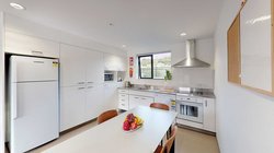 Matipo, Titoki and Tānekaha apartments' kitchen with fridge, bench top, oven and a dining table with chairs