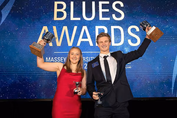 Two students holding up silver trophies on stage at the Blues Awards