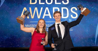 Two students holding up silver trophies on stage at the Blues Awards
