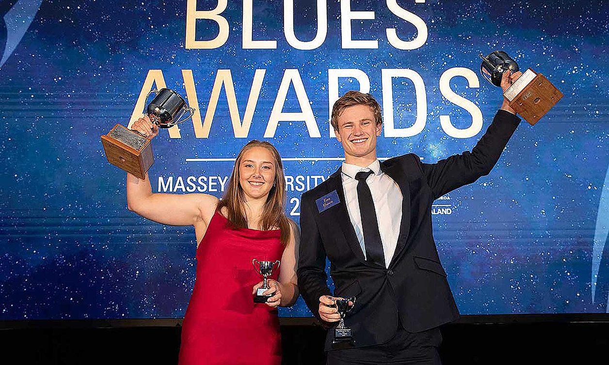 Two students holding up silver trophies on stage at the Blues Awards