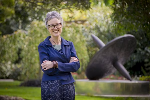 Professor Giselle Byrnes standing on the Manawatū campus, smiling with her arms folded.