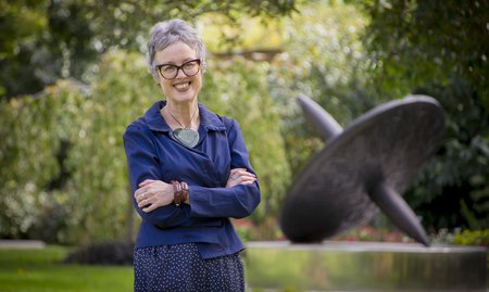 Professor Giselle Byrnes standing on the Manawatū campus, smiling with her arms folded.