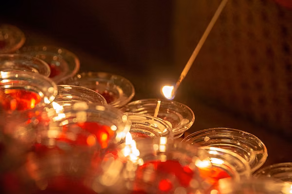Close-up of a multitude of candles in small glass holders, with one being lit