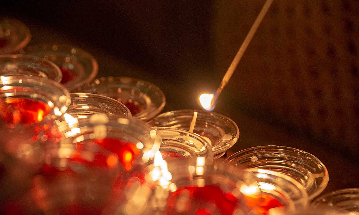 Close-up of a multitude of candles in small glass holders, with one being lit