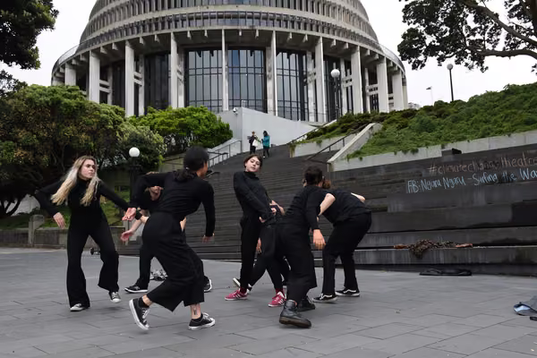 A group of young performers engaging in climate change street theatre on the steps of the New Zealand Parliament. The Beehive is in the background.