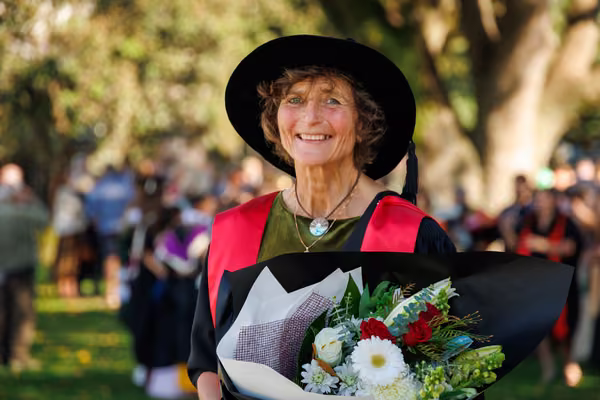 woman smiling at camera in graduation gown holding flowers
