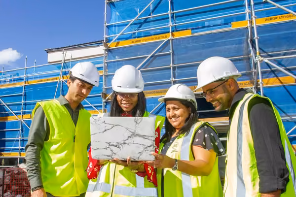 Four people in high vis inspect a laptop at a construction site