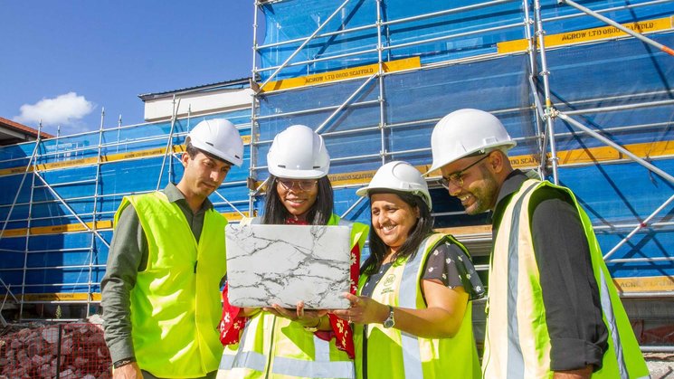 Four people in high vis inspect a laptop at a construction site