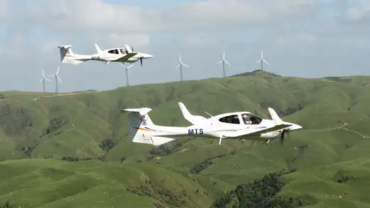 Diamond aircraft in flight with wind turbines in background