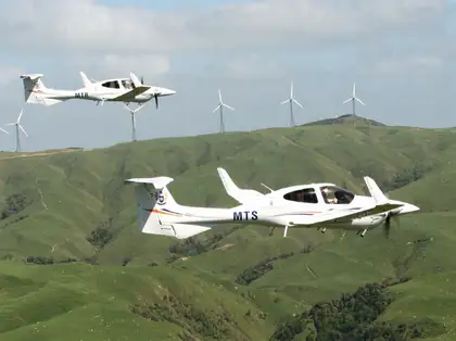 Diamond aircraft in flight with wind turbines in background