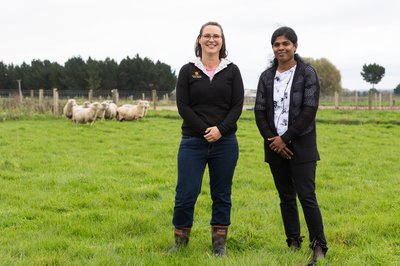 Two women standing in a paddock with sheep in background.