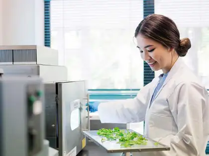 Smiling person in lab coat puts plant samples in a machine