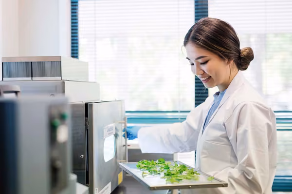 Smiling person in lab coat puts plant samples in a machine