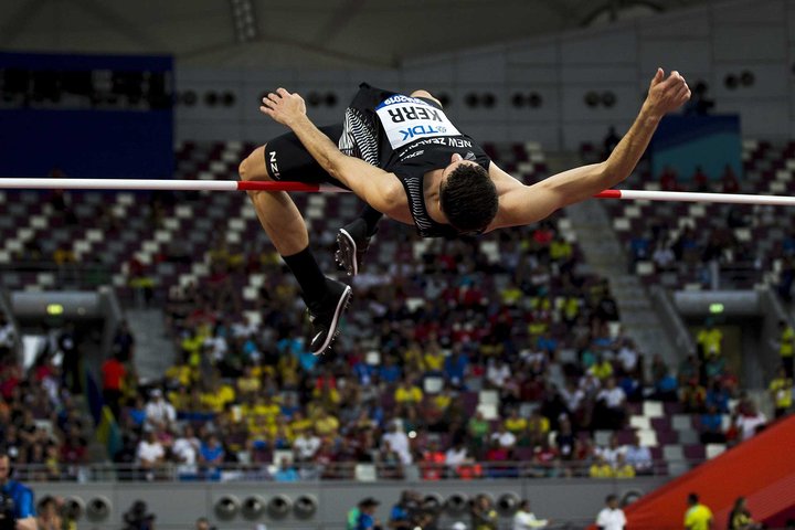 Athlete in mid-air over the high jump, with a crowd seated in the stands