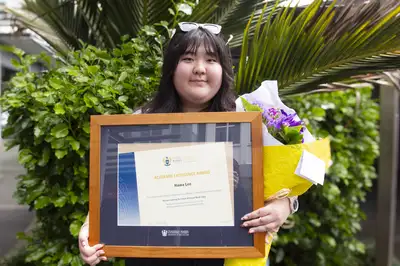 Hawa Lee standing outside with her flowers and framed award.