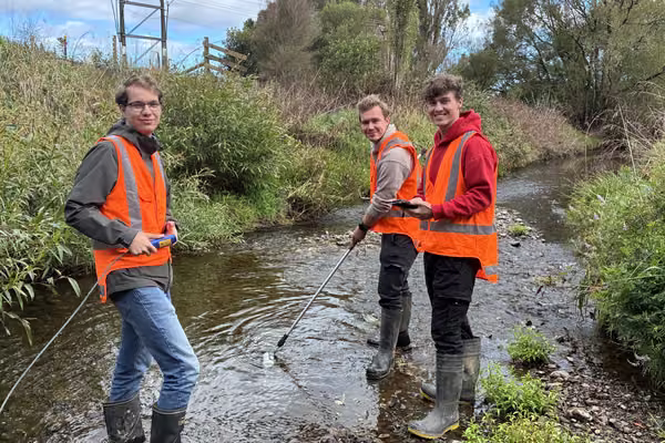 three men in high-vis vests standing in a stream smiling