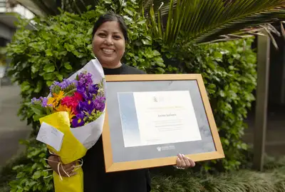 Jacinta Saldanha standing outside with her flowers and framed award.