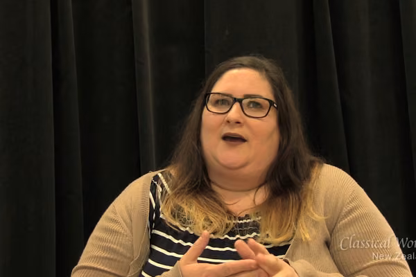 Woman caught mid sentence. Wearing glasses and a striped top.