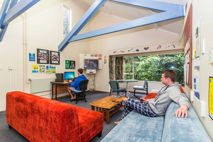 Interior of Kiwitea accommodation lounge, with students relaxing on couch and sitting at a computer