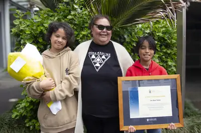 Lee-Anne Tatana standing with her mokopuna holding flowers and her framed award.